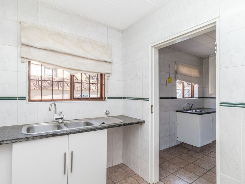 A functional scullery area featuring tiled walls, granite countertops, and a double stainless steel sink, with an adjacent secondary prep space visible.
