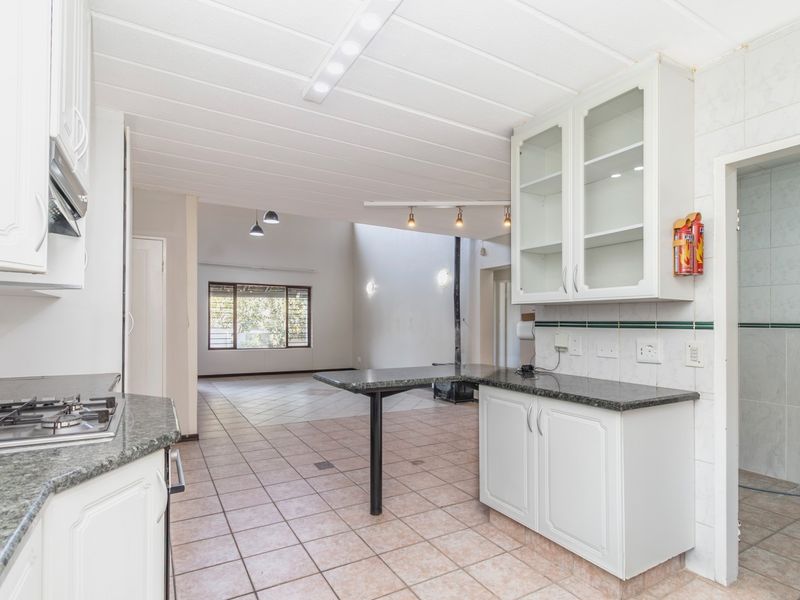 Spacious open-plan kitchen and living area featuring granite countertops, gas cooktop, built-in cabinetry, and a central fireplace, finished with neutral floor tiles.