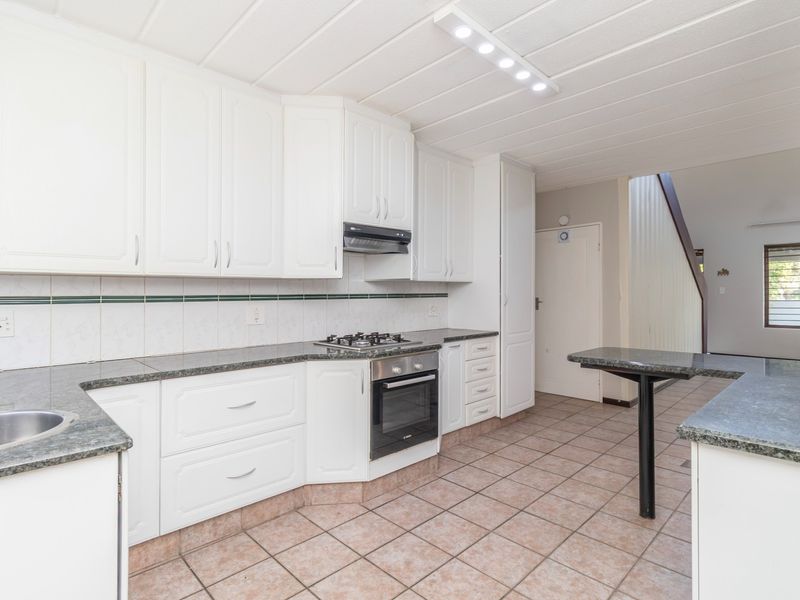 A functional kitchen featuring white cabinetry, granite countertops, a gas hob, built-in oven, and tiled flooring, offering a clean and practical workspace.