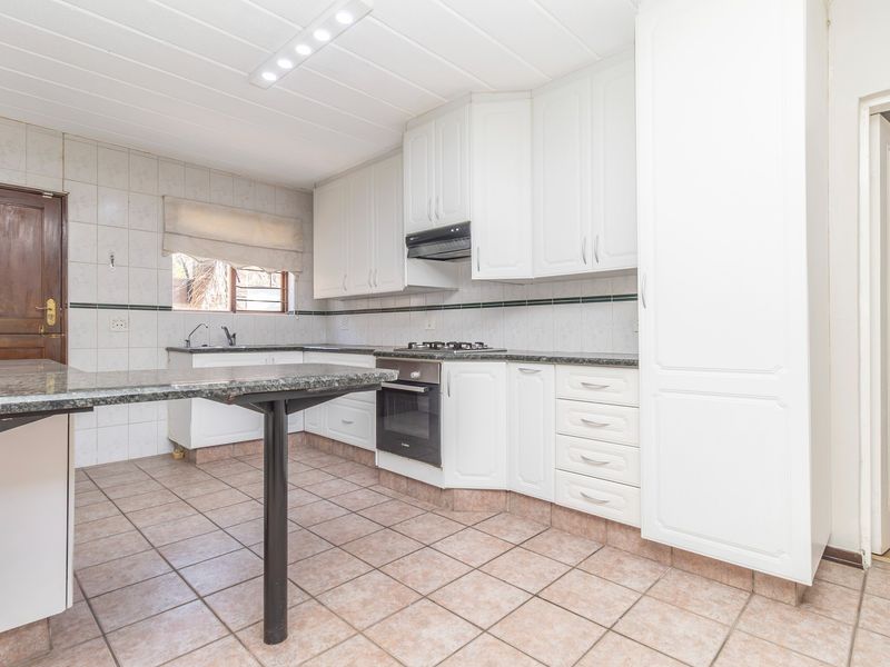 A functional kitchen featuring white cabinetry, granite countertops, built-in oven, gas hob, and tiled flooring, offering a clean and practical workspace.