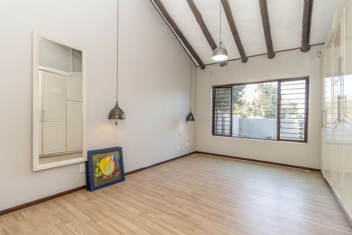 Spacious bedroom featuring high vaulted ceilings with exposed timber beams, laminate flooring, and extensive built-in cupboard storage.