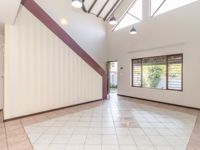 Spacious living area featuring high vaulted ceilings with exposed rafters, large windows for natural light, and neutral ceramic tile flooring.