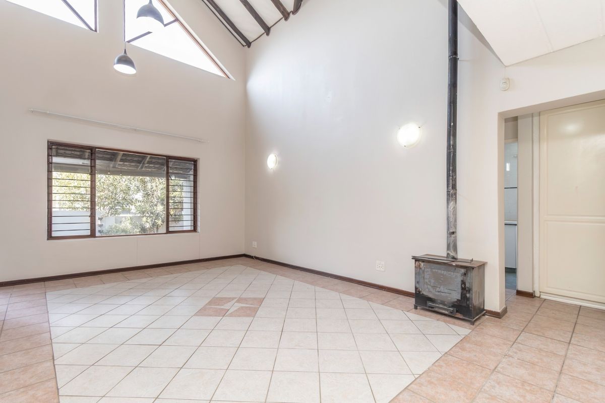 Spacious living area featuring a high vaulted ceiling with exposed rafters, tiled flooring, and a central freestanding fireplace.