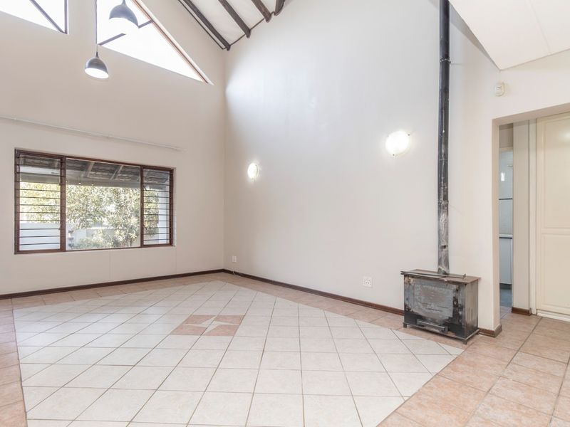 Spacious living area featuring a high vaulted ceiling with exposed rafters, tiled flooring, and a central freestanding fireplace.