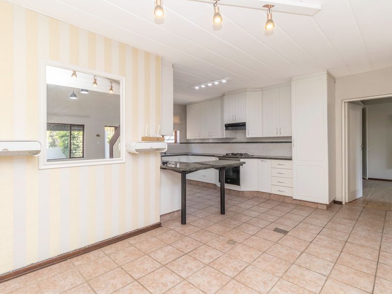 A spacious kitchen featuring white built-in cabinetry, granite countertops, a gas hob, and a convenient pass-through window connecting to the adjacent living area.