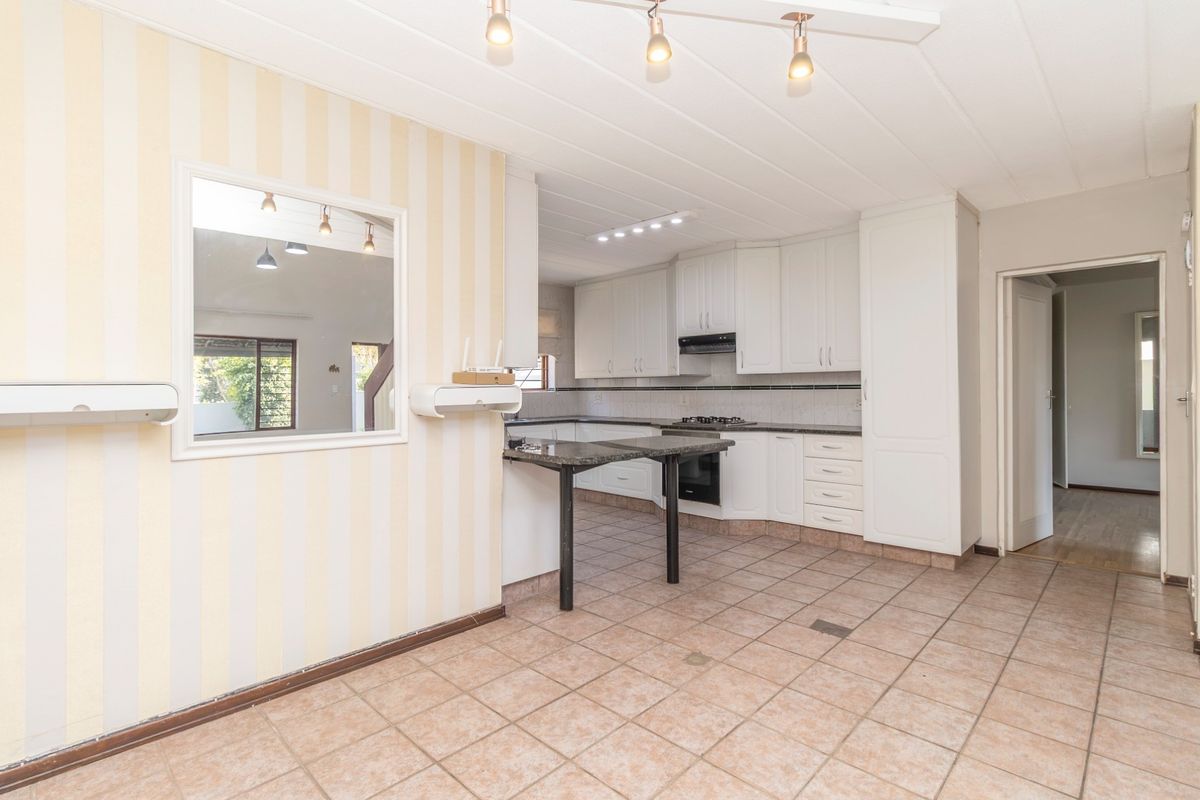 A spacious kitchen featuring white built-in cabinetry, granite countertops, a gas hob, and a convenient pass-through window connecting to the adjacent living area.