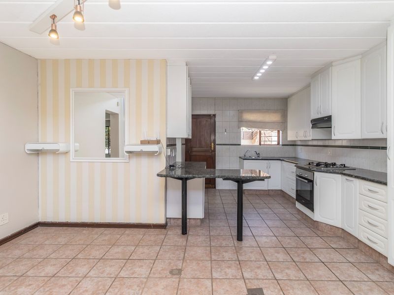 A functional kitchen featuring white cabinetry, granite countertops, a gas hob, and a breakfast bar, with tiled flooring throughout.