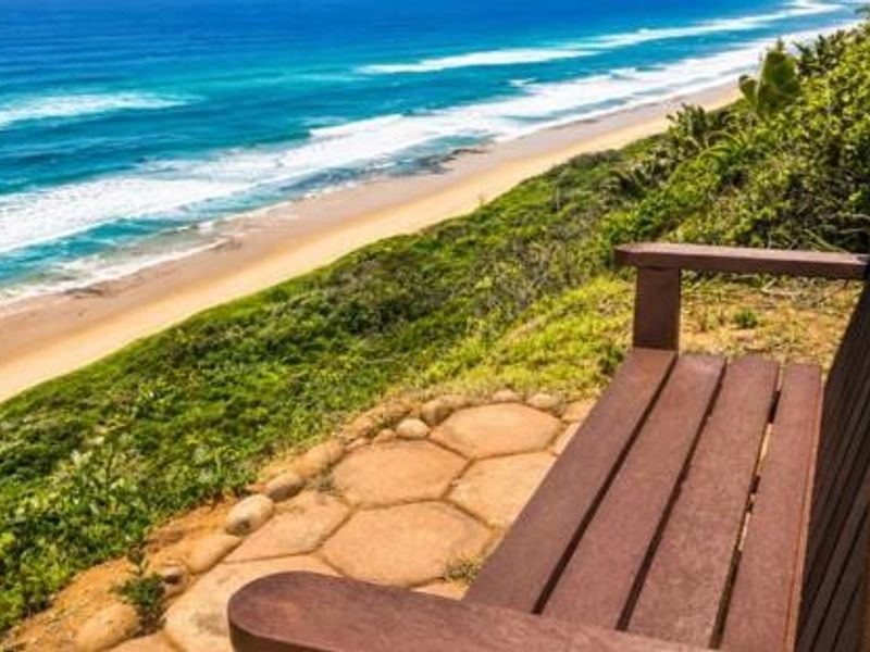 A scenic coastal view overlooking the ocean and sandy beach from a paved outdoor seating area.