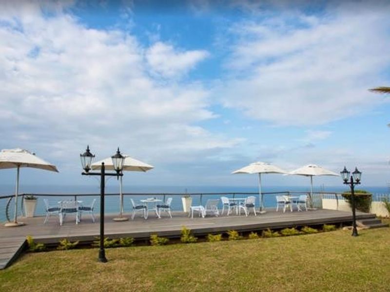 Elevated timber deck patio featuring a metal balustrade, garden lighting, and expansive ocean views, set within a well-maintained lawn area.