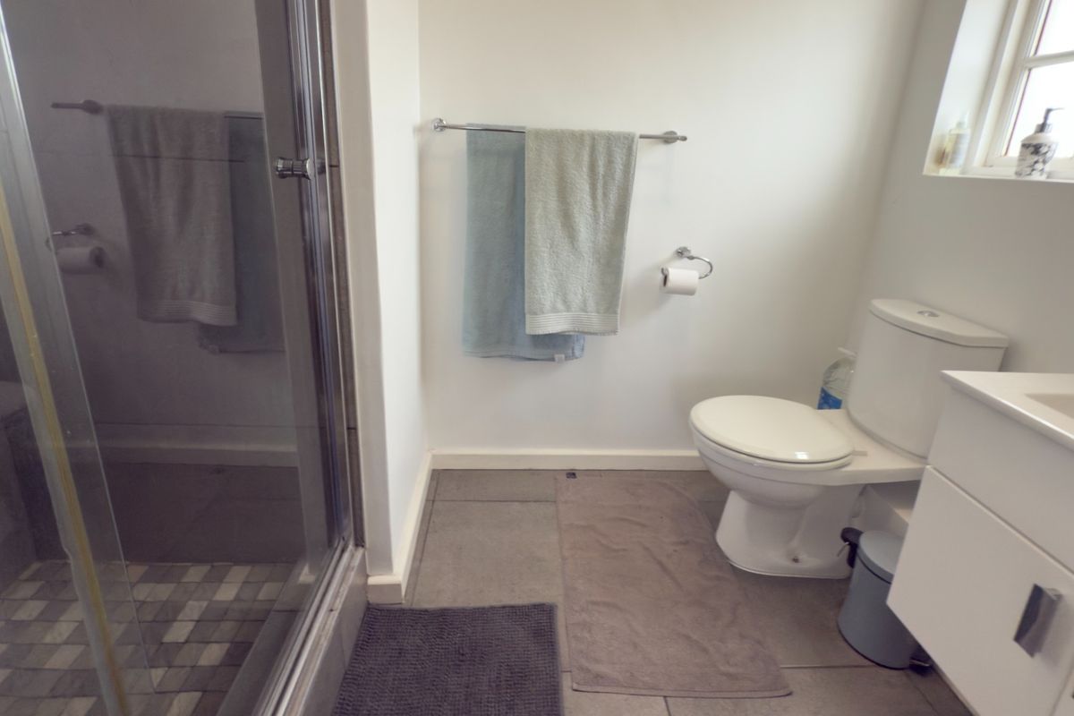 A functional bathroom featuring a glass-enclosed shower, a modern vanity cabinet, and a standard toilet with tiled flooring.