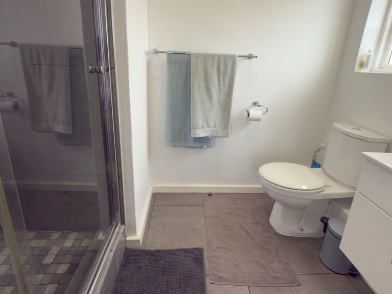 A functional bathroom featuring a glass-enclosed shower, a modern vanity cabinet, and a standard toilet with tiled flooring.