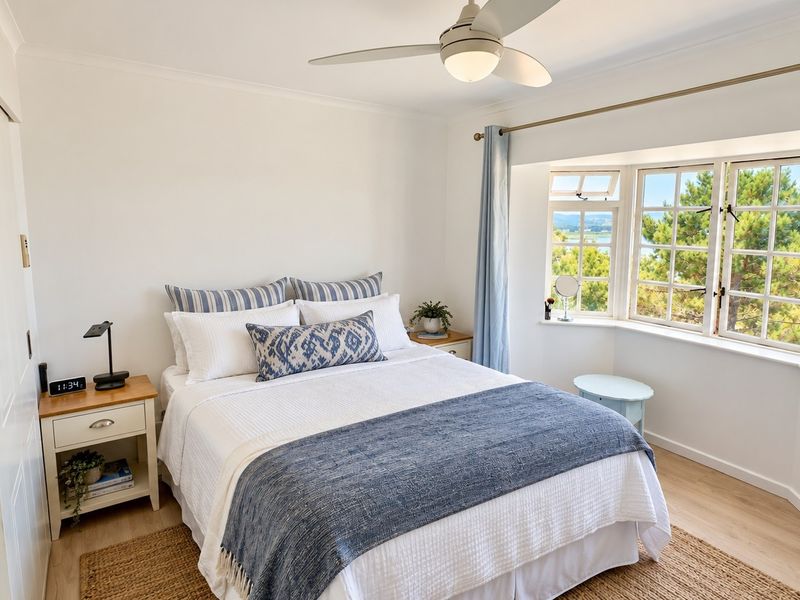 A bright and well-maintained bedroom featuring a ceiling fan, built-in wardrobe, and a large bay window offering scenic views.