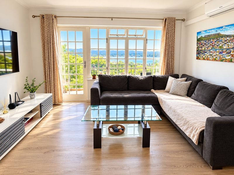 A bright and well-maintained living room featuring laminate flooring, a wall-mounted air conditioner, and large french doors offering scenic views.