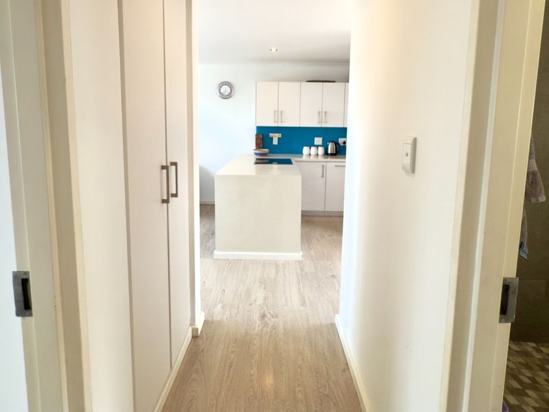 A view through a hallway into an open-plan kitchen area featuring modern cabinetry, a central island, and light-toned laminate flooring.