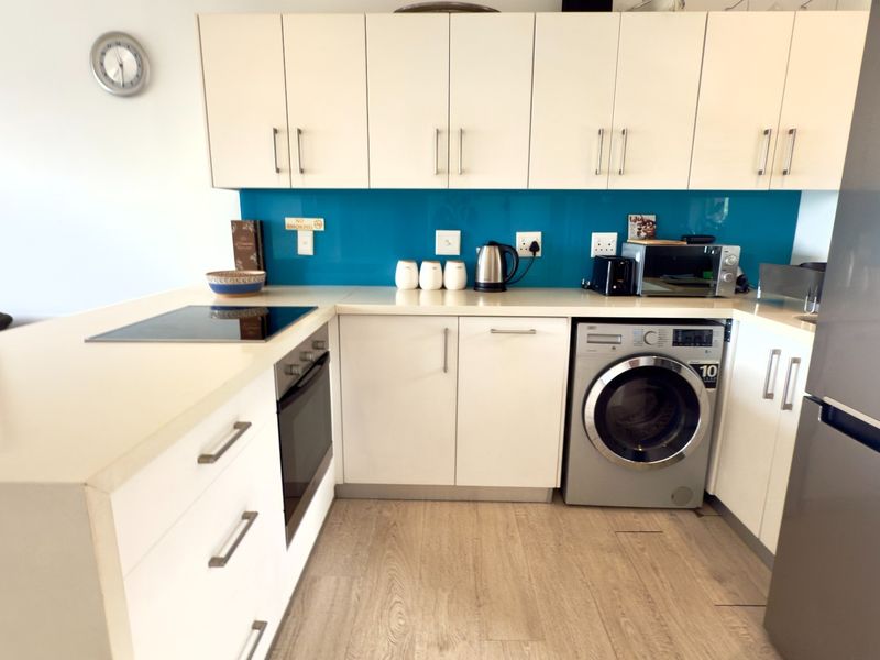 Modern kitchen featuring white cabinetry, a vibrant blue glass splashback, stone countertops, integrated oven, electric cooktop, and a built-in washing machine.
