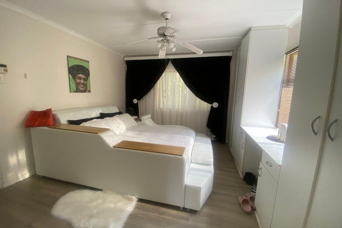 A well-maintained bedroom featuring laminate flooring, a ceiling fan, and ample built-in cupboard storage with integrated desk space.