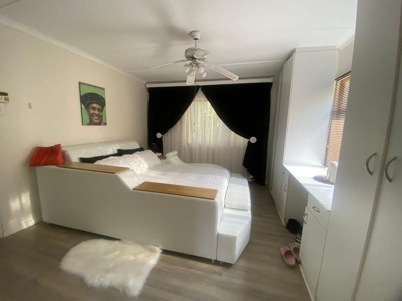 A well-maintained bedroom featuring laminate flooring, a ceiling fan, and ample built-in cupboard storage with integrated desk space.