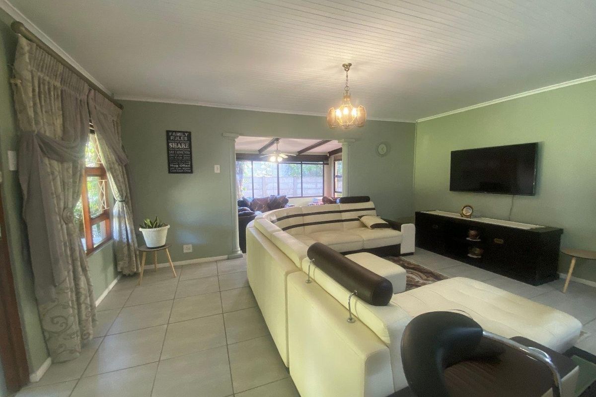 A spacious living room featuring tiled flooring, a tongue and groove ceiling, and a wall-mounted television, with an open transition to an adjacent living area.