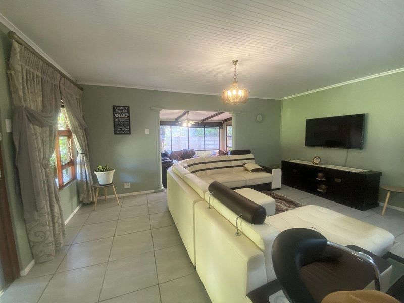 A spacious living room featuring tiled flooring, a tongue and groove ceiling, and a wall-mounted television, with an open transition to an adjacent living area.