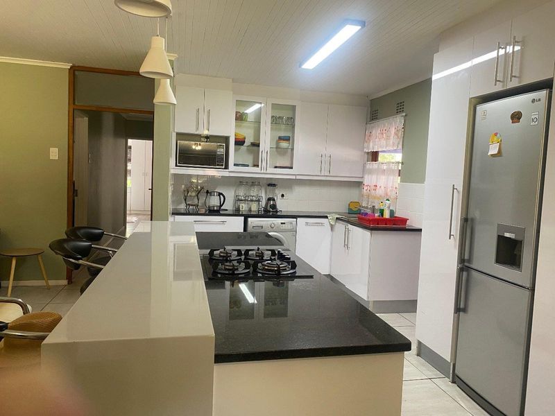 A functional kitchen featuring white cabinetry, a central island with a gas hob, stone countertops, and tiled flooring.