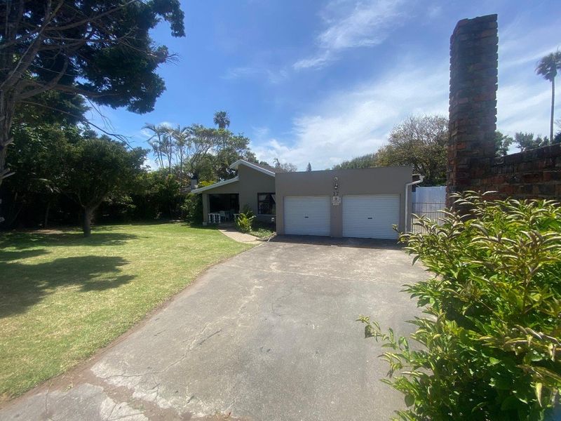 Front view of the property featuring a double garage, concrete driveway, and established garden with a prominent brick chimney.