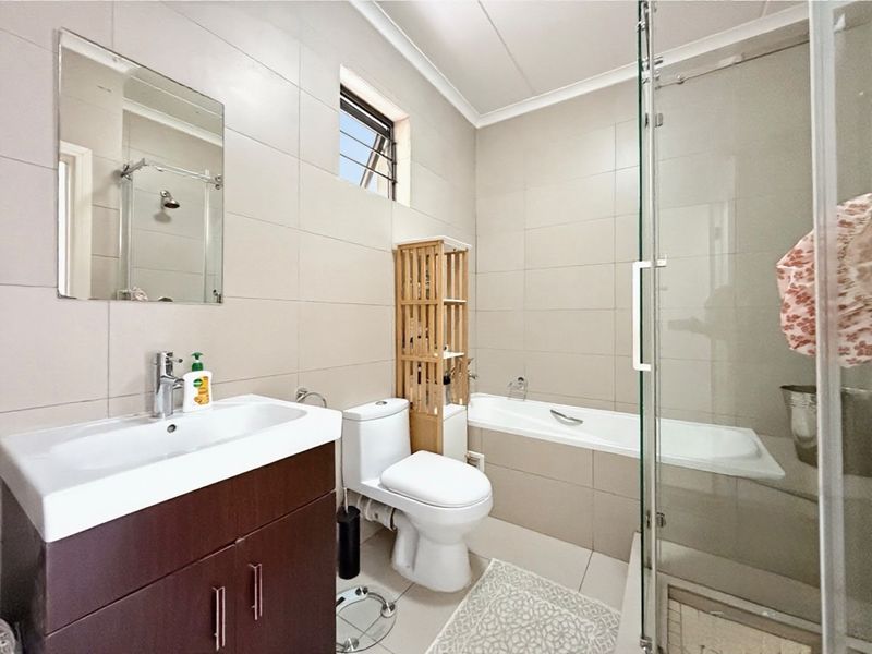 A well-maintained bathroom featuring a vanity cabinet, a separate bathtub, and a glass-enclosed shower with neutral wall and floor tiling.