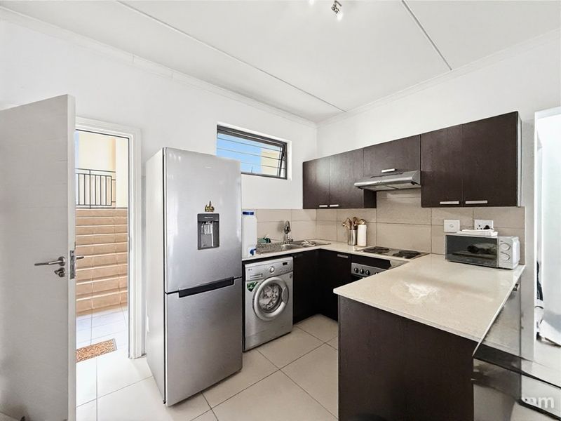 A functional kitchen featuring dark wood cabinetry, stone countertops, integrated hob, extractor fan, and tiled flooring, with direct access to an outdoor area.