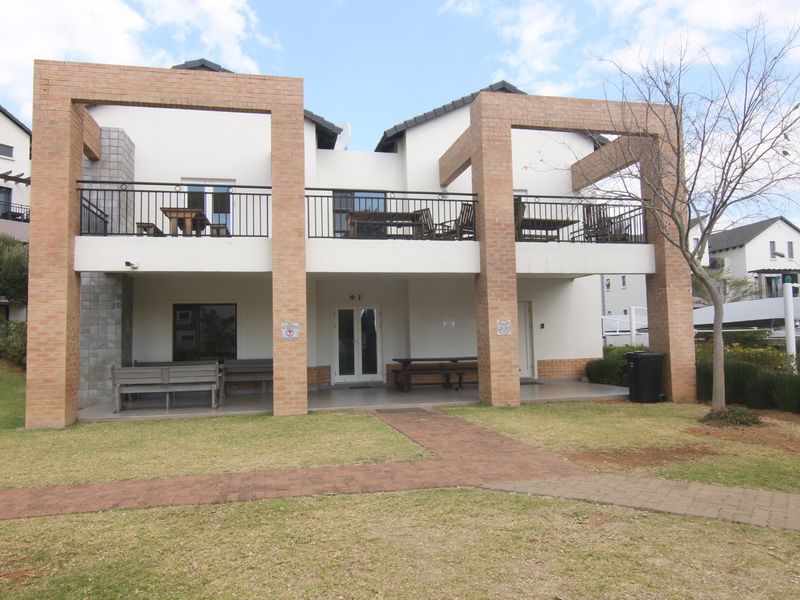 Rear view of the apartment building featuring a covered ground floor patio, an upper-level balcony with metal railings, and brick structural pillars.