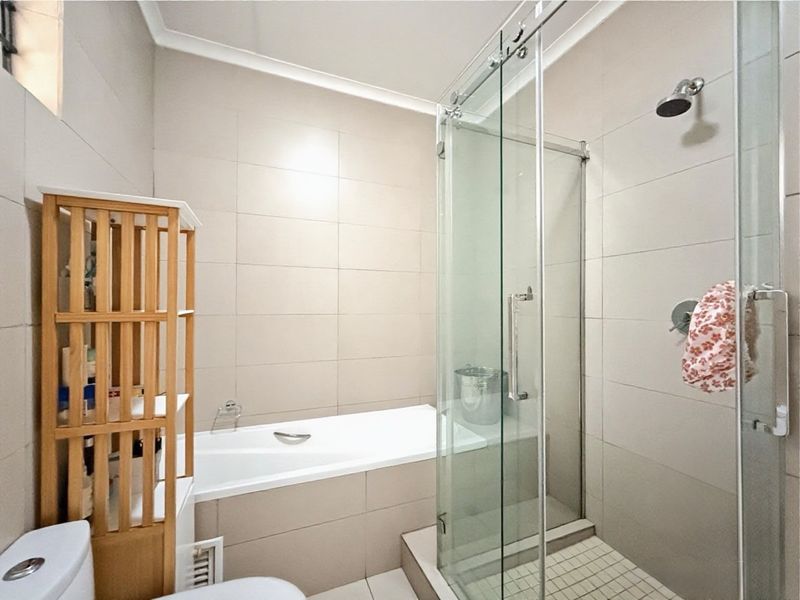 A modern bathroom featuring a built-in bathtub, a separate glass-enclosed shower, and neutral wall tiling.