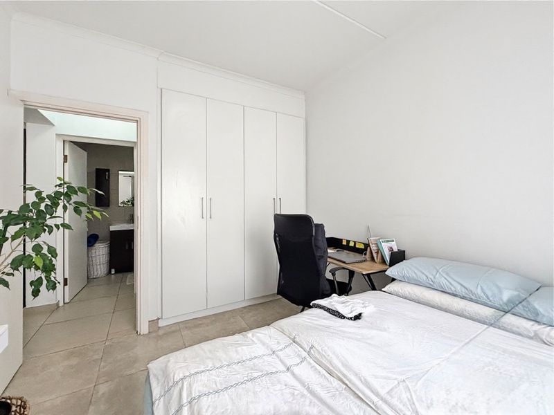 A functional bedroom featuring built-in cupboards, tiled flooring, and direct access to an en-suite bathroom.