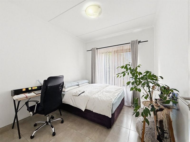 A well-lit bedroom featuring neutral tiled flooring and a large window with curtain rod, providing a clean and functional living space.