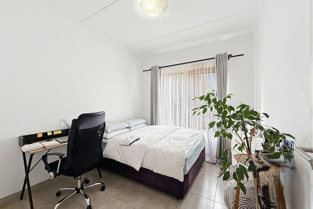 A well-lit bedroom featuring neutral tiled flooring and a large window with curtain rod, providing a clean and functional living space.