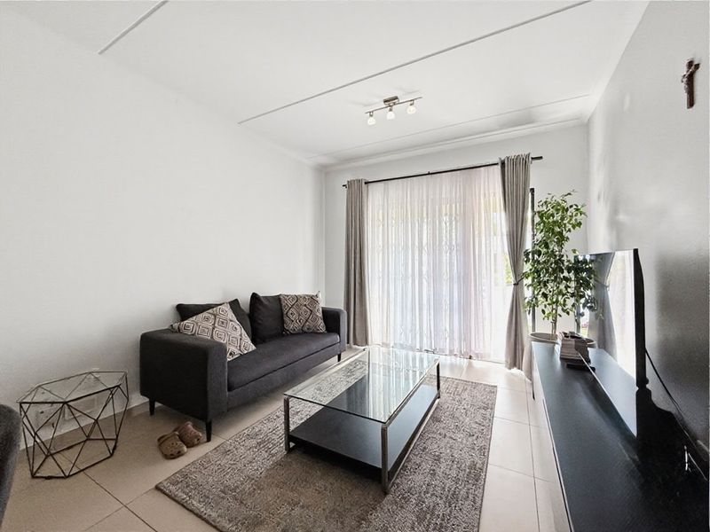 A bright and well-maintained living room featuring neutral tiled flooring and a large sliding glass door that provides access to the outdoor area.