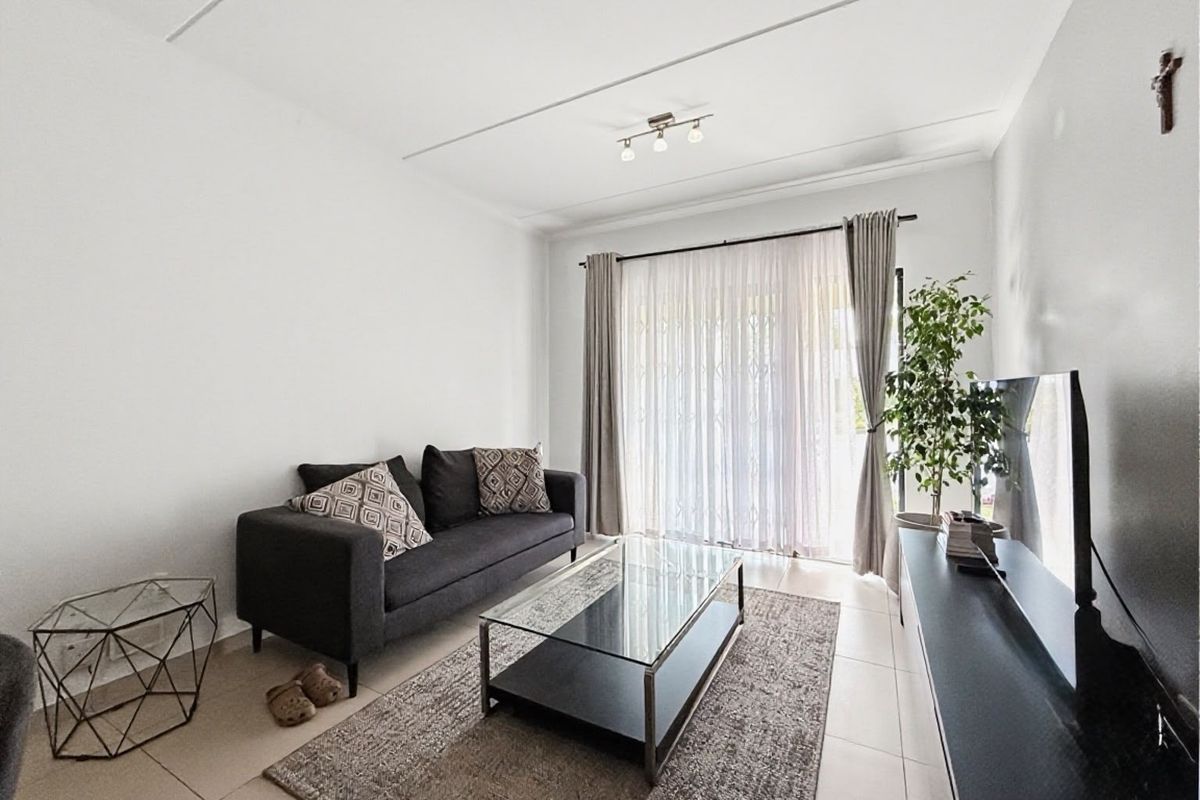 A bright and well-maintained living room featuring neutral tiled flooring and a large sliding glass door that provides access to the outdoor area.