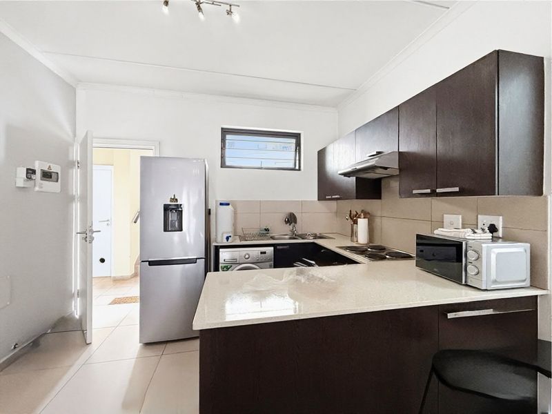 A functional kitchen featuring dark wood cabinetry, stone countertops, a tiled backsplash, and integrated appliances, offering a clean and modern aesthetic.