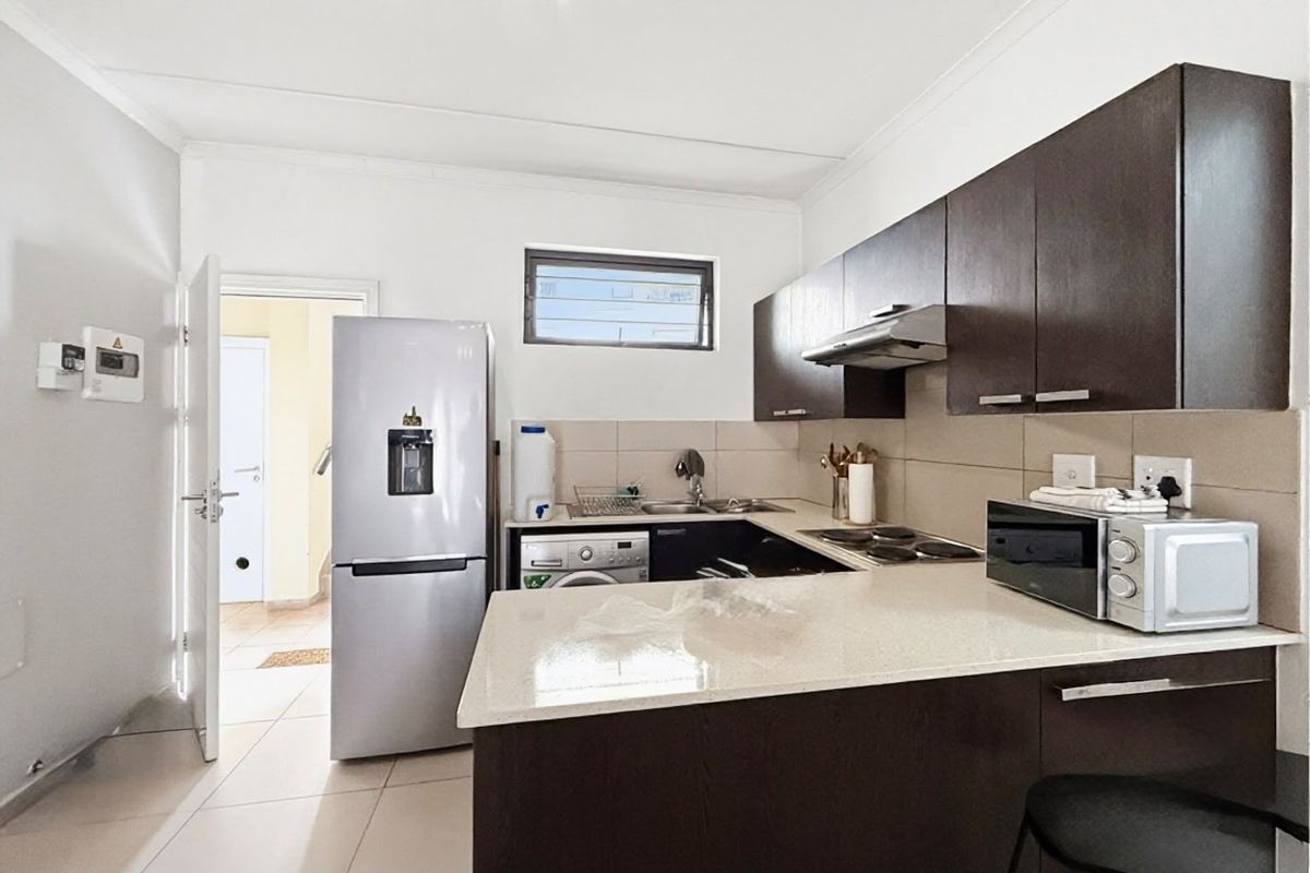 A functional kitchen featuring dark wood cabinetry, stone countertops, a tiled backsplash, and integrated appliances, offering a clean and modern aesthetic.