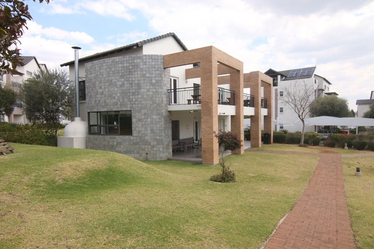 Rear view of the apartment building featuring a landscaped lawn, paved walkway, brick structural pillars, and a balcony with metal railings.