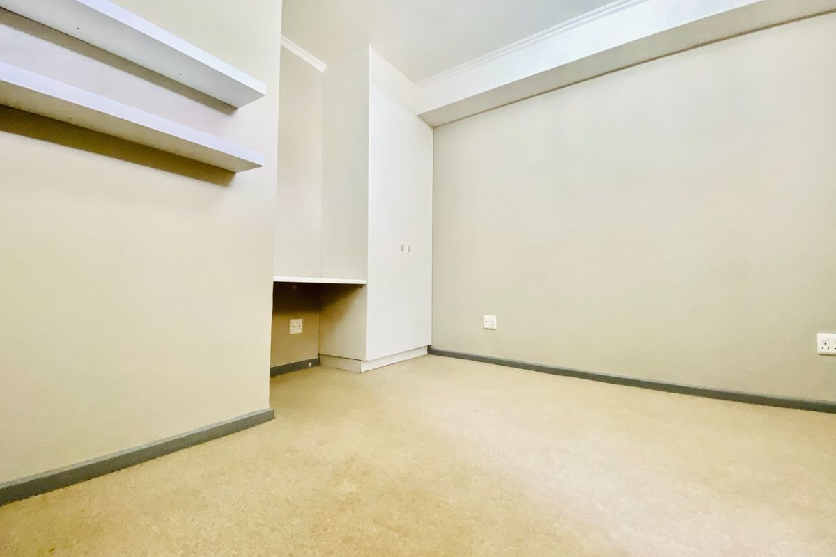 An empty bedroom featuring neutral walls, carpet flooring, built-in wardrobe, integrated desk space, and floating shelves.