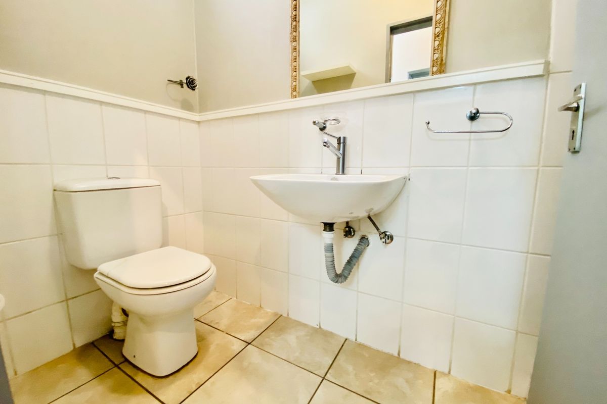 A functional bathroom featuring a wall-mounted basin, standard toilet, and tiled finishes throughout.