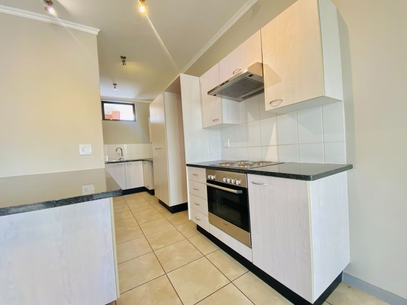 A clean, functional kitchen featuring light-toned cabinetry, granite countertops, built-in oven, electric hob, and tiled flooring.