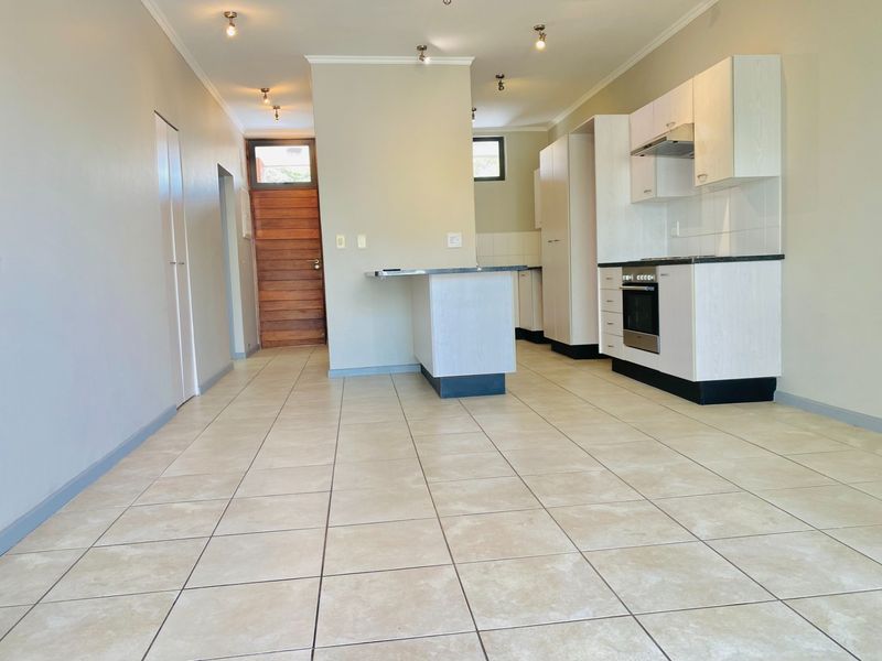 An open-plan living and kitchen area featuring neutral tiled flooring, modern built-in cabinetry, an integrated oven, and a breakfast counter.