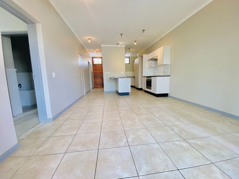 An open-plan living and kitchen area featuring neutral tiled flooring, built-in cabinetry, and a functional kitchen island in a clean, vacant space.