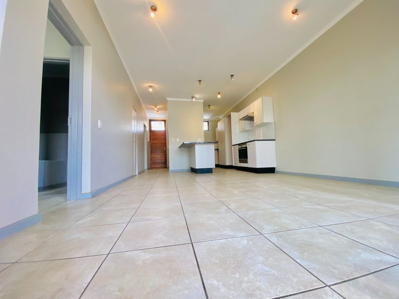 Spacious open-plan living and kitchen area featuring neutral tiled flooring, modern white cabinetry, built-in oven, and a functional kitchen island.