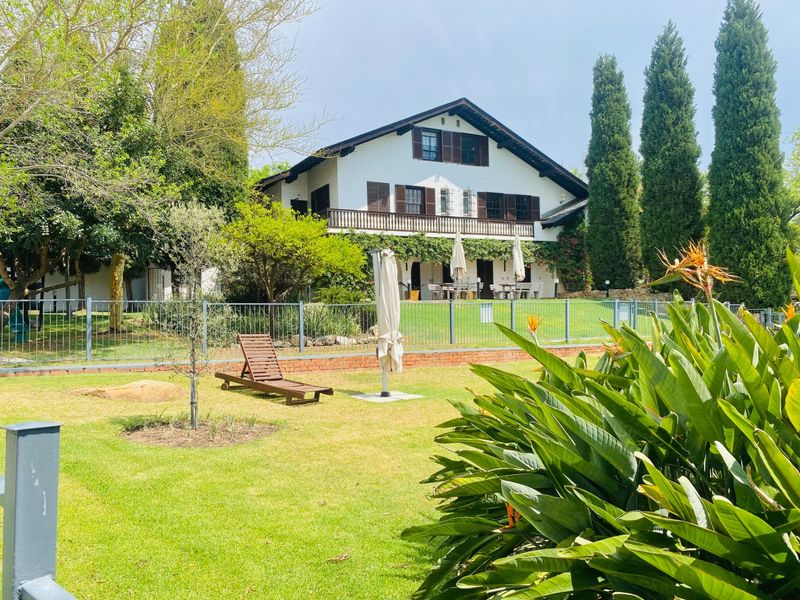 A view of the rear elevation of a two-story residence featuring a balcony, timber shutters, and a well-maintained garden with metal fencing.