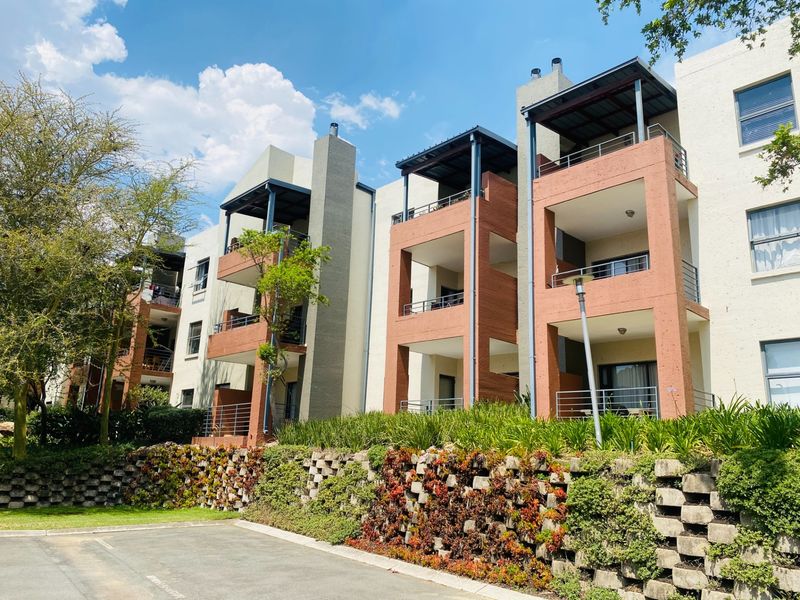 Rear elevation of a multi-story apartment complex featuring private balconies, integrated chimney stacks, and a landscaped retaining wall above a paved parking area.