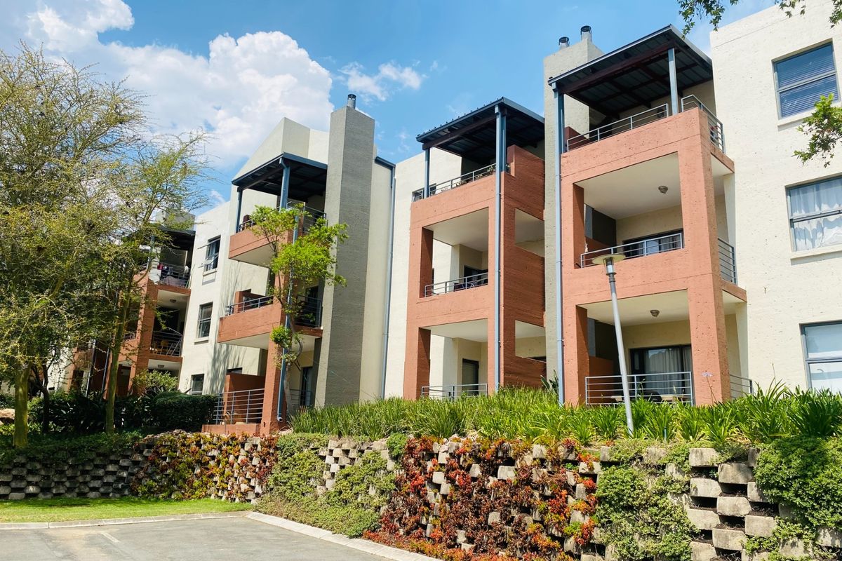 Rear elevation of a multi-story apartment complex featuring private balconies, integrated chimney stacks, and a landscaped retaining wall above a paved parking area.