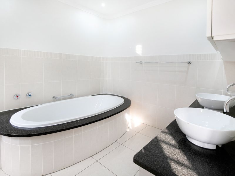 A clean, modern bathroom featuring a built-in bathtub with a granite surround and a double vanity with vessel sinks.
