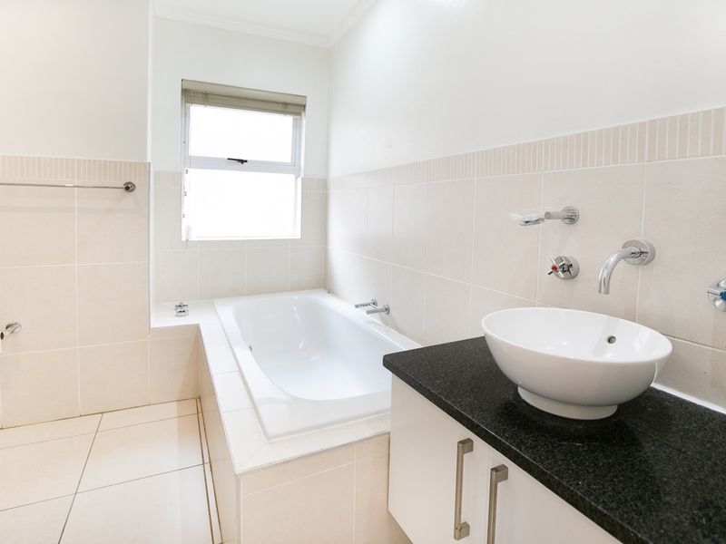 A clean, modern bathroom featuring a built-in bathtub, a vessel sink on a granite vanity, and neutral wall and floor tiling.