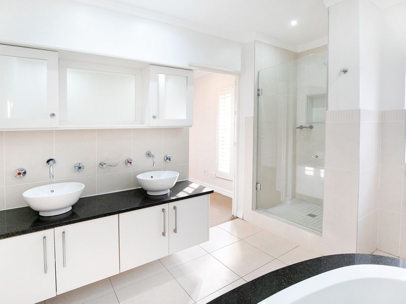 Modern bathroom featuring a double vanity with vessel sinks, granite countertops, and a spacious glass-enclosed shower with neutral wall and floor tiling.