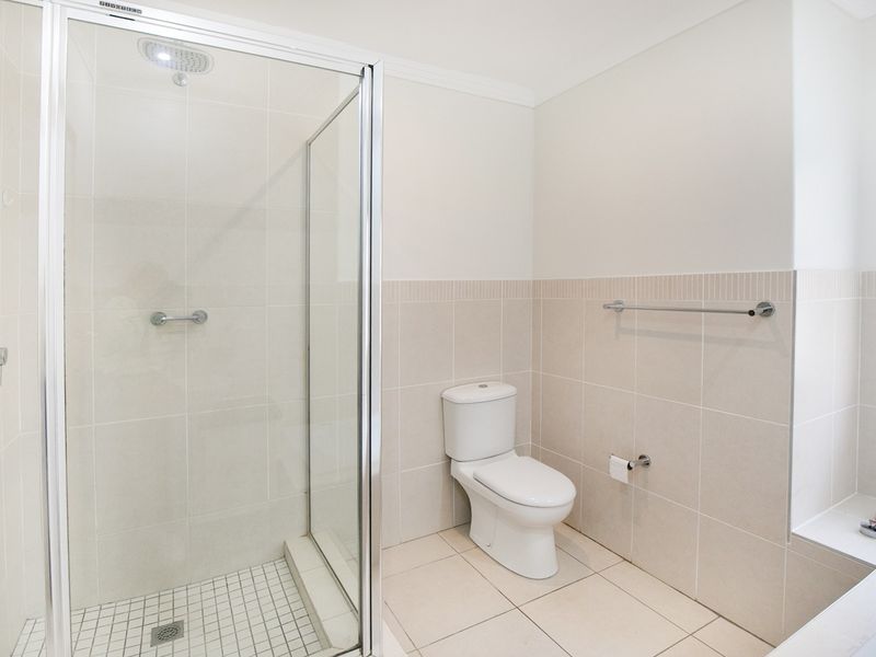 A clean, modern bathroom featuring a glass-enclosed shower, a separate bathtub, and neutral floor-to-ceiling tiling.